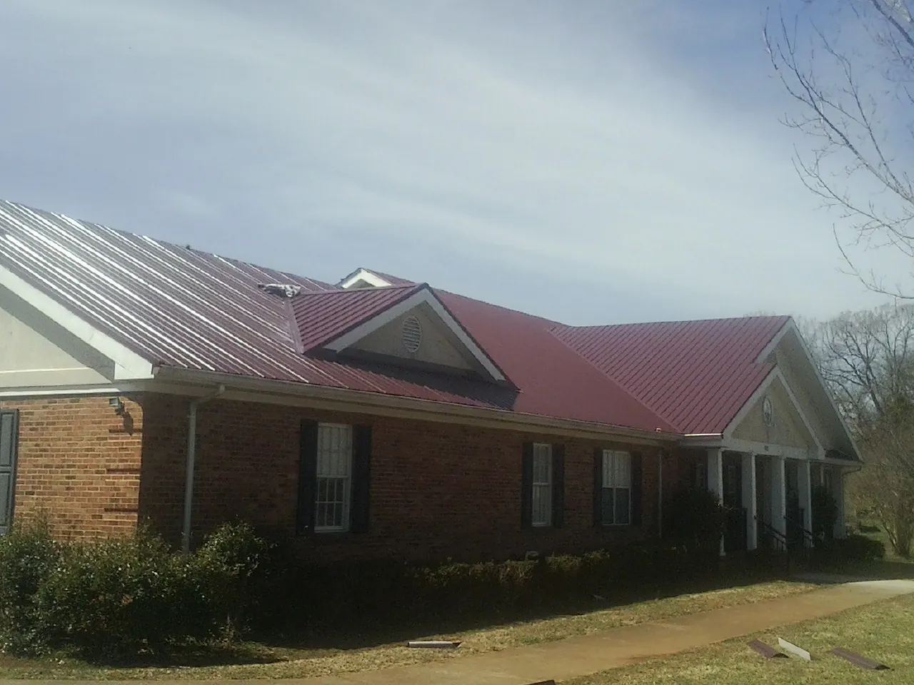 Red metal roof with gabled entries on a long brick building, from a Hail Damage Roof Repair job in Allerton