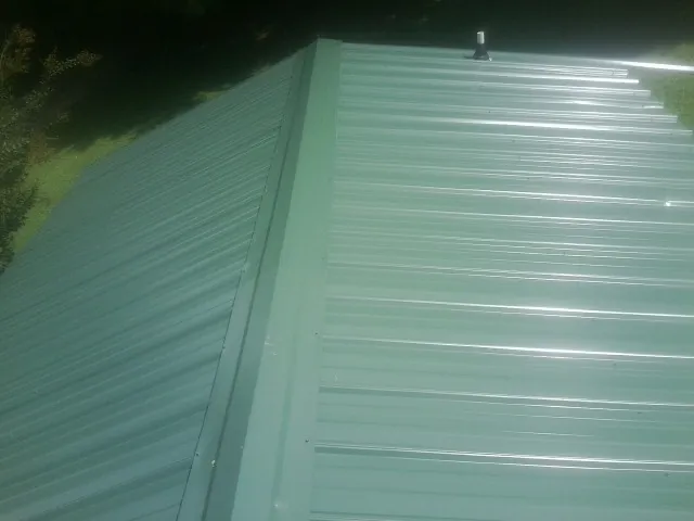 New green metal panels meeting at the ridge of a roof — Flat Roof Repair work by our crew in Allerton