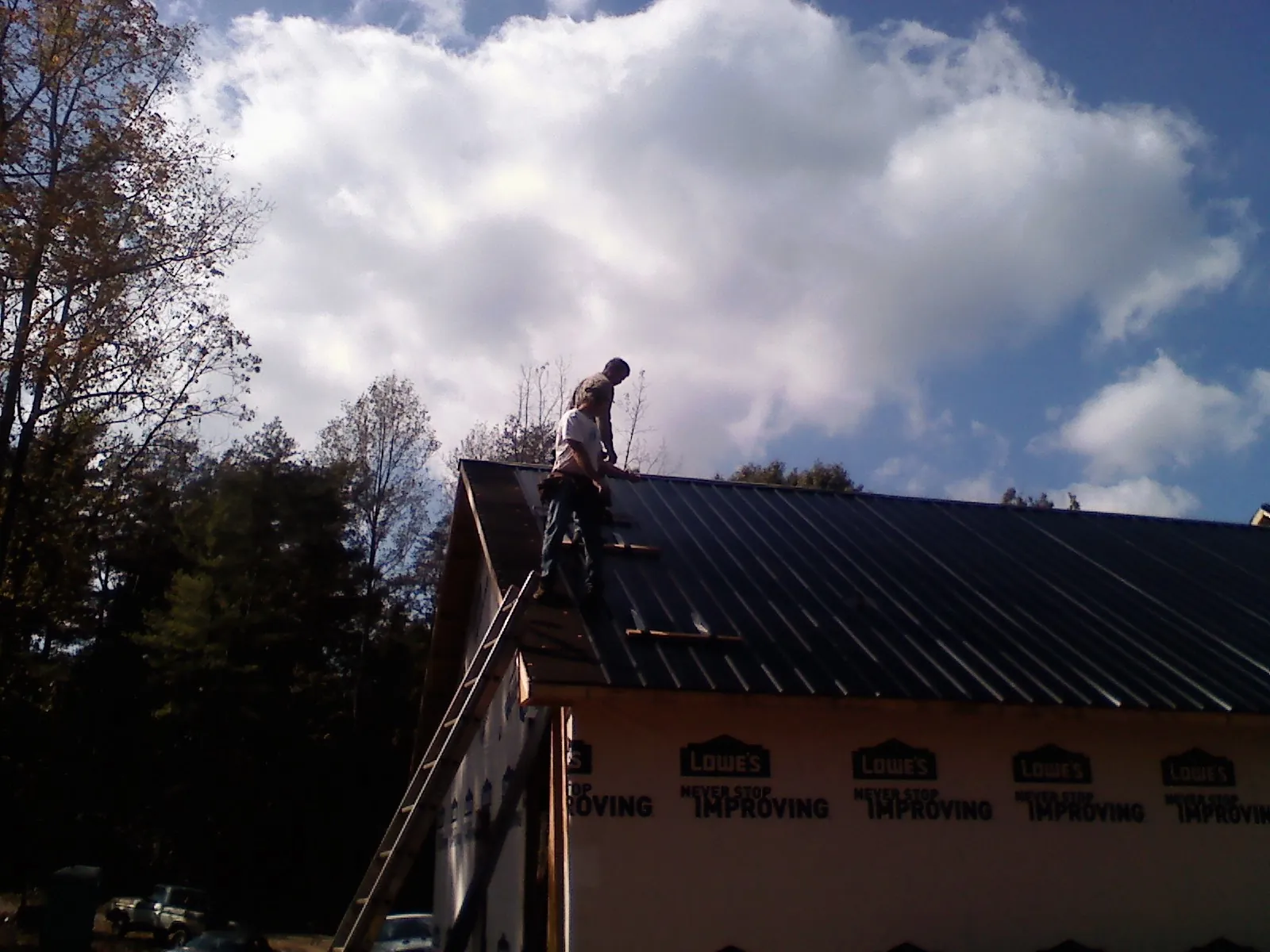 Roofer fastening dark metal panels high against a cloudy sky, from a Roof Inspection job in Allerton