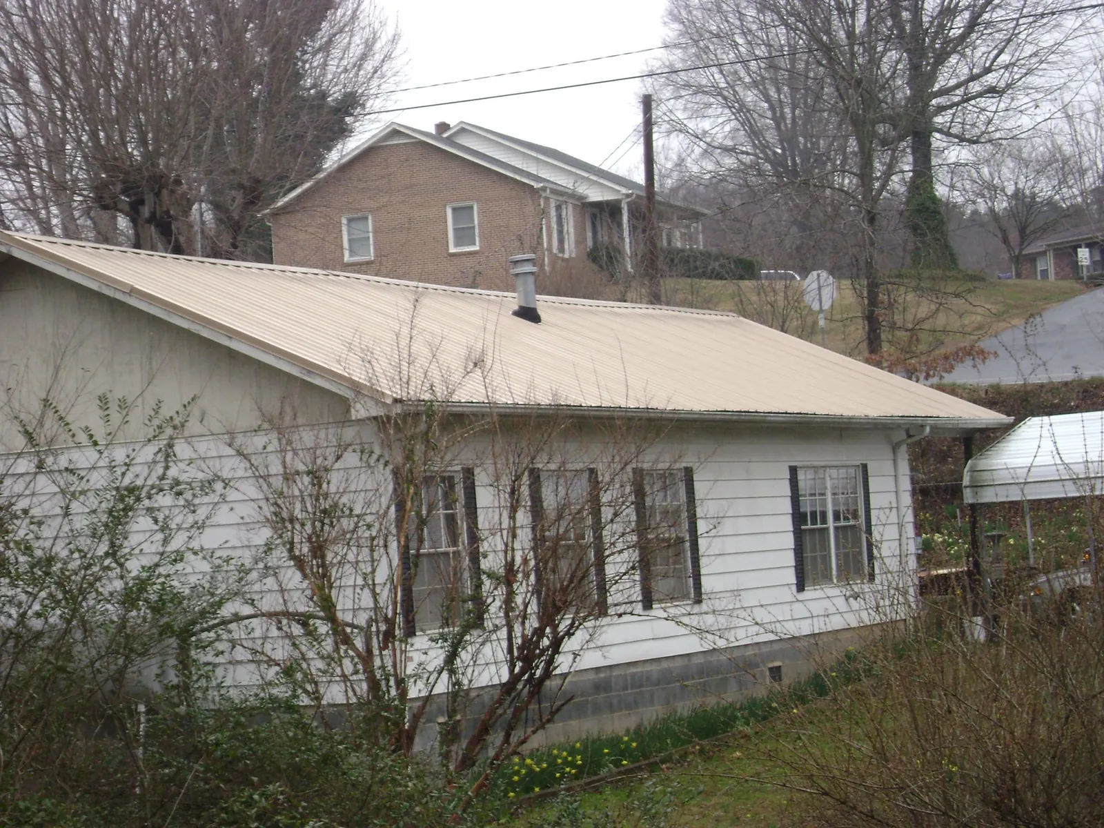 Tan metal roof on a white sided house set into a hillside — Commercial Roofing by Roofing Brothers in Allerton