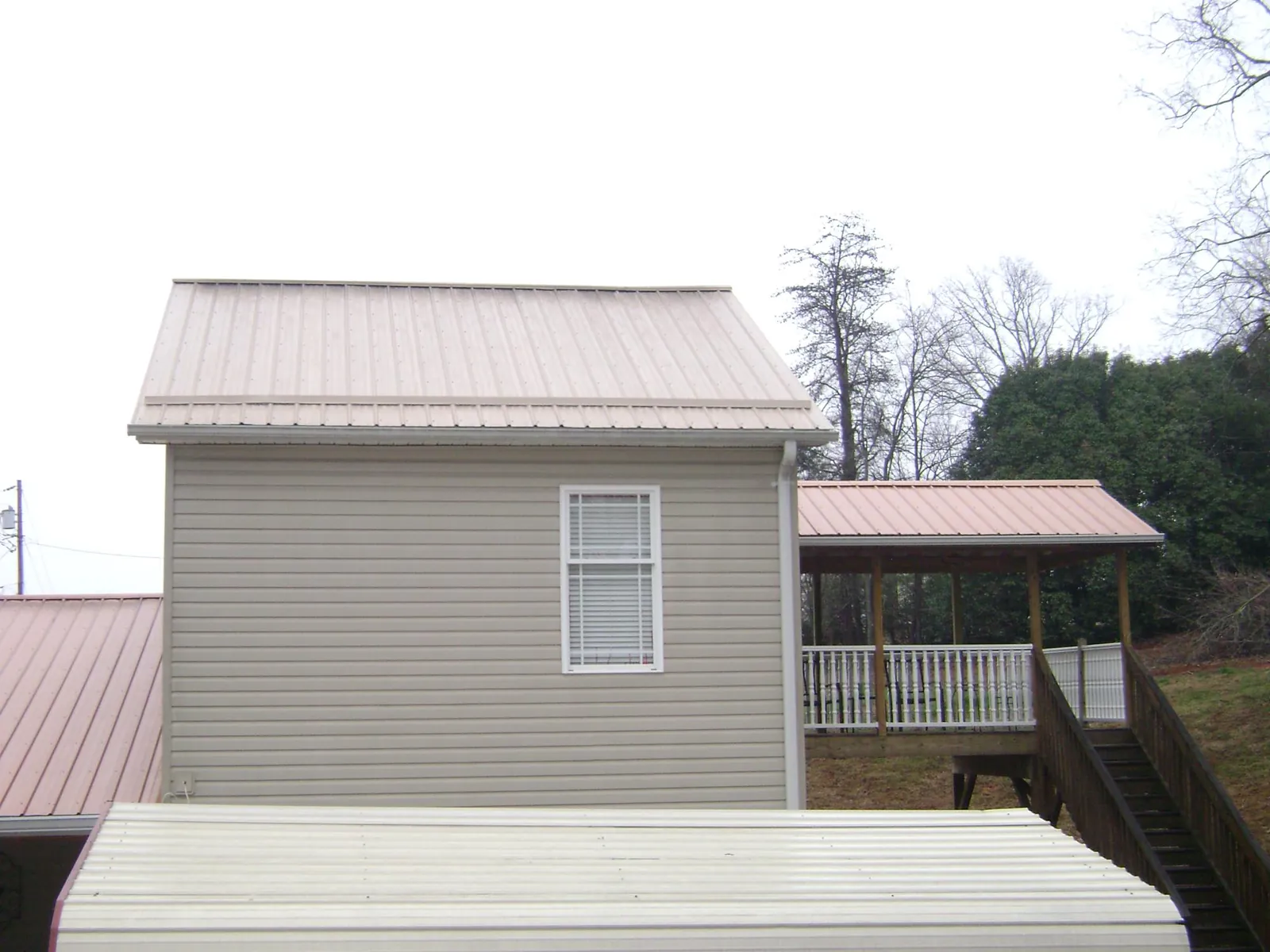 Tan metal roofs on a two story addition and attached porch, from a Roof Replacement job in Allerton